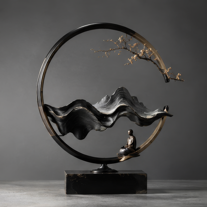 DINOVIR circular Zen mountain sculpture with seated monk and gold-tone blossom branch on a rectangular base against a plain gray background